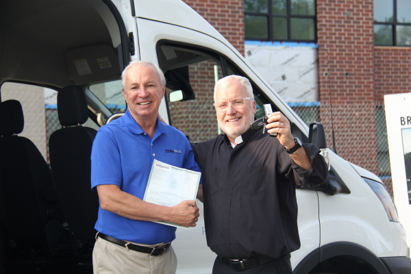Dave Brown, General Manager of MobilityTRANS, presenting the title and keys of a new Ford E-Transit to Fr. Tim McCabe, Executive Director of the Pope Francis Center, in a handover event on Tuesday.
